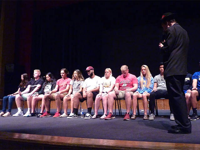 Long row of students on stage get hypnotized at a Chicago area high school graduation hypnosis show.
