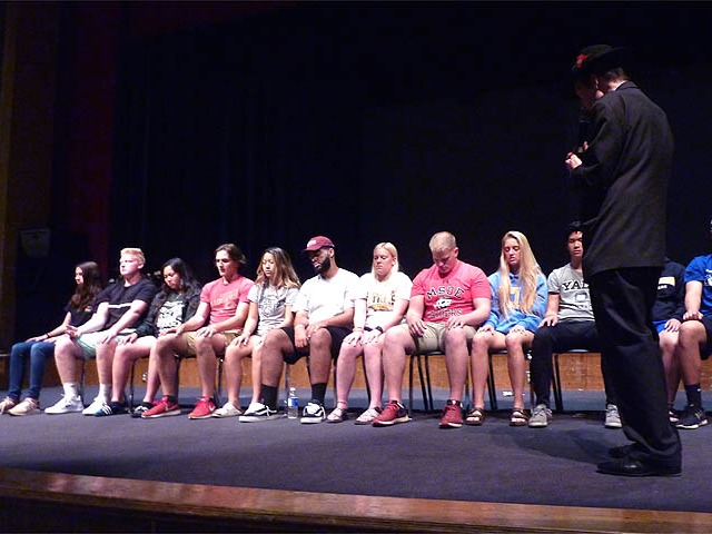Long row of students on stage get hypnotized at a Chicago area high school graduation hypnosis show.